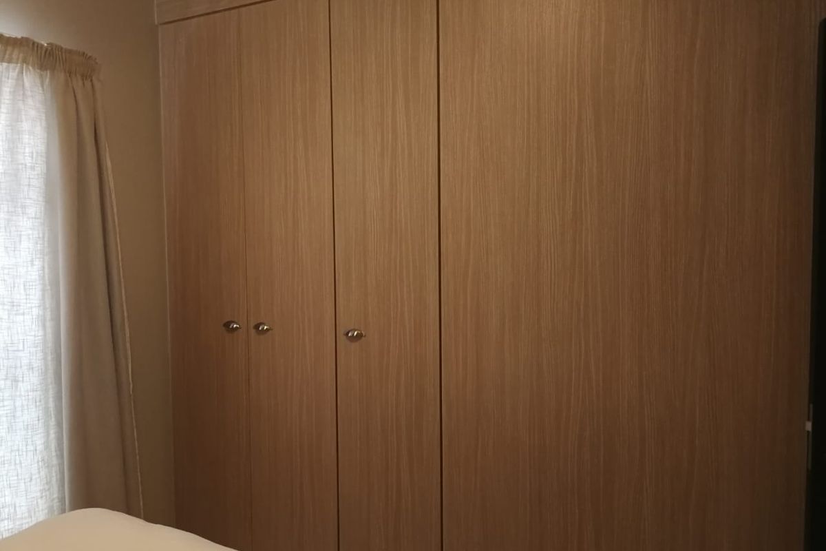 A bedroom featuring floor-to-ceiling built-in wooden cupboards with a clean, modern finish.