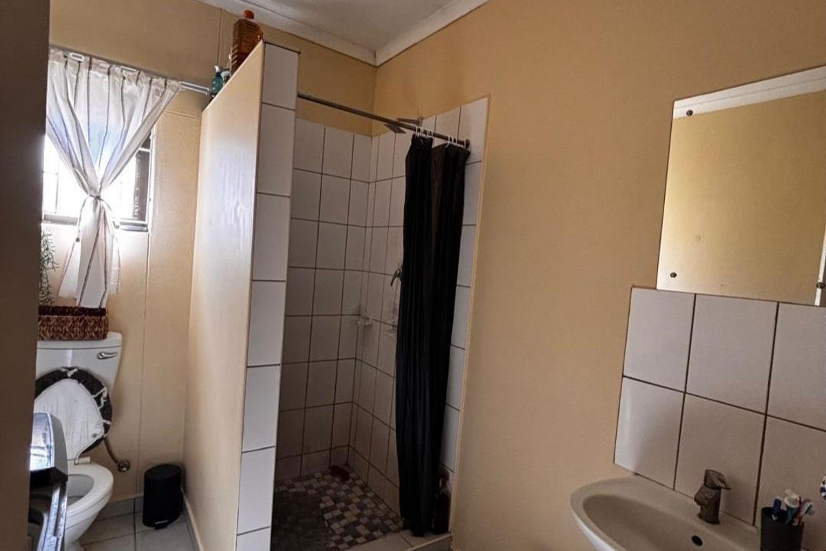 A functional bathroom featuring a walk-in shower with tiled surround, a wall-mounted basin, and a standard toilet.