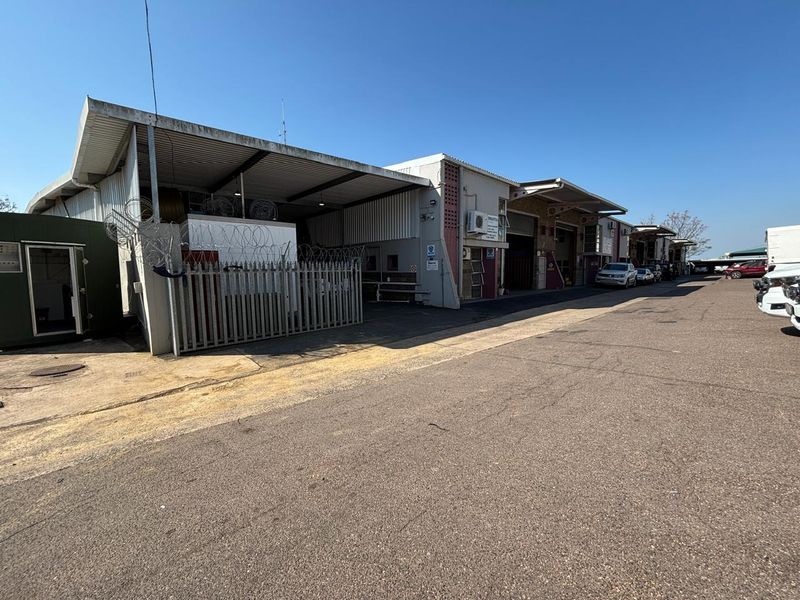 Industrial property exterior featuring multiple covered loading bays, security fencing with razor wire, and an expansive asphalt driveway for vehicle access.