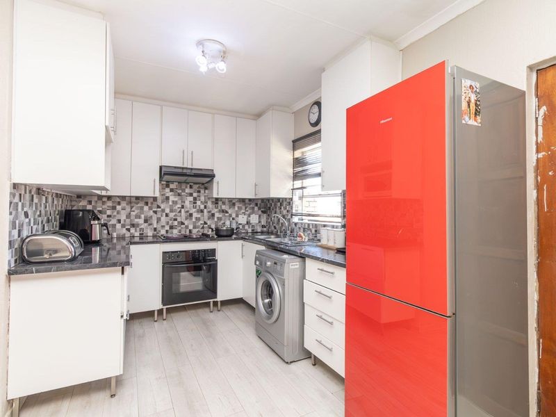 A functional kitchen featuring white cabinetry, dark laminate countertops, a tiled backsplash, and integrated cooking appliances with light-toned laminate flooring.