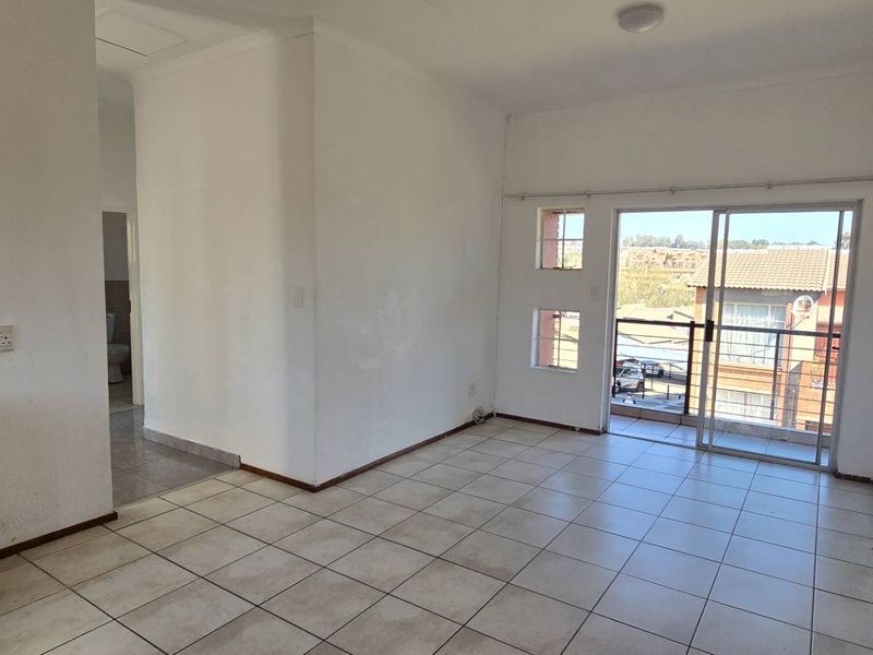 Open-plan living area featuring tiled floors, a compact kitchen corner, and a sliding glass door leading to a balcony.