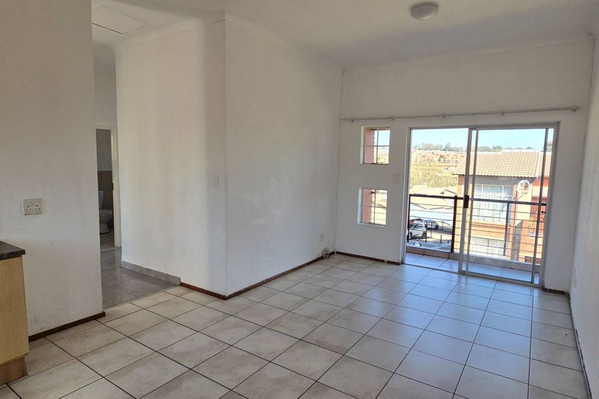 Open-plan living area featuring tiled floors, a compact kitchen corner, and a sliding glass door leading to a balcony.