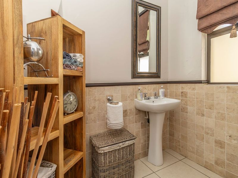 A functional bathroom featuring a pedestal basin, neutral wall tiles, and tiled flooring, providing a clean and practical space.