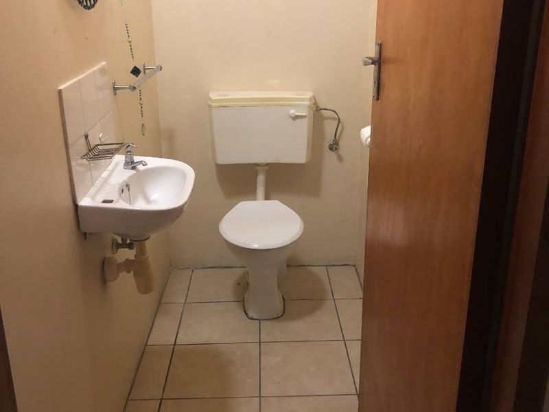 A compact guest bathroom featuring a wall-mounted basin and a standard toilet with tiled flooring and splashback.