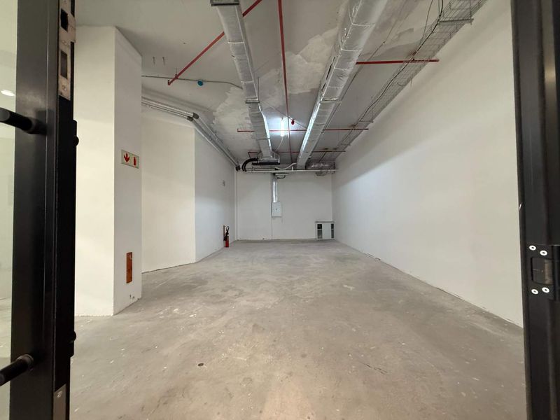 An empty, industrial-style utility space featuring exposed ceiling ductwork, cable trays, and concrete flooring, suitable for storage or commercial fit-out.