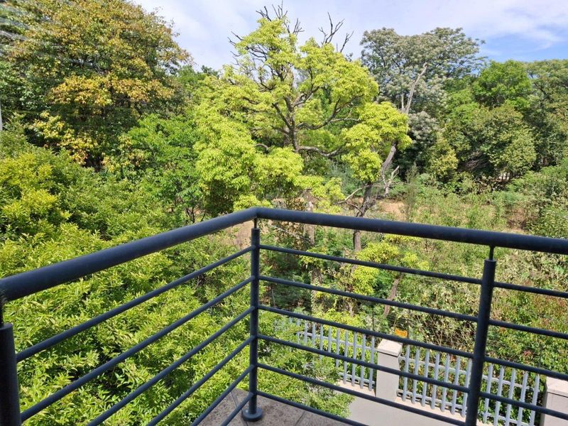 A private balcony featuring a modern metal balustrade, offering a peaceful, elevated view of the surrounding lush green trees and natural landscape.
