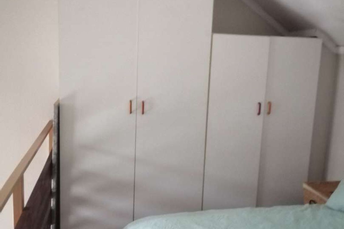 Bedroom featuring built-in white wardrobes and a sloped ceiling, with a wooden balustrade overlooking the lower level.