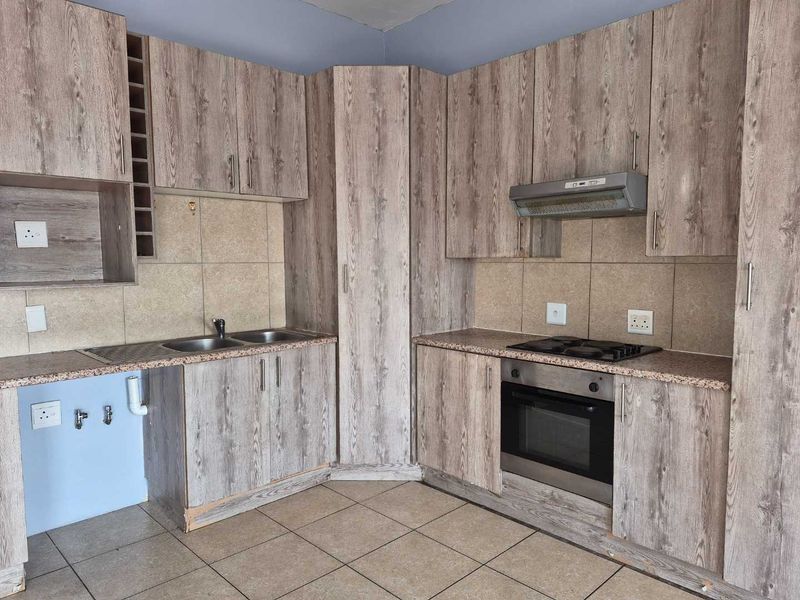 A functional kitchen featuring wood-look laminate cabinetry, built-in oven, gas hob, extractor fan, and tiled flooring, offering a practical layout for culinary needs.