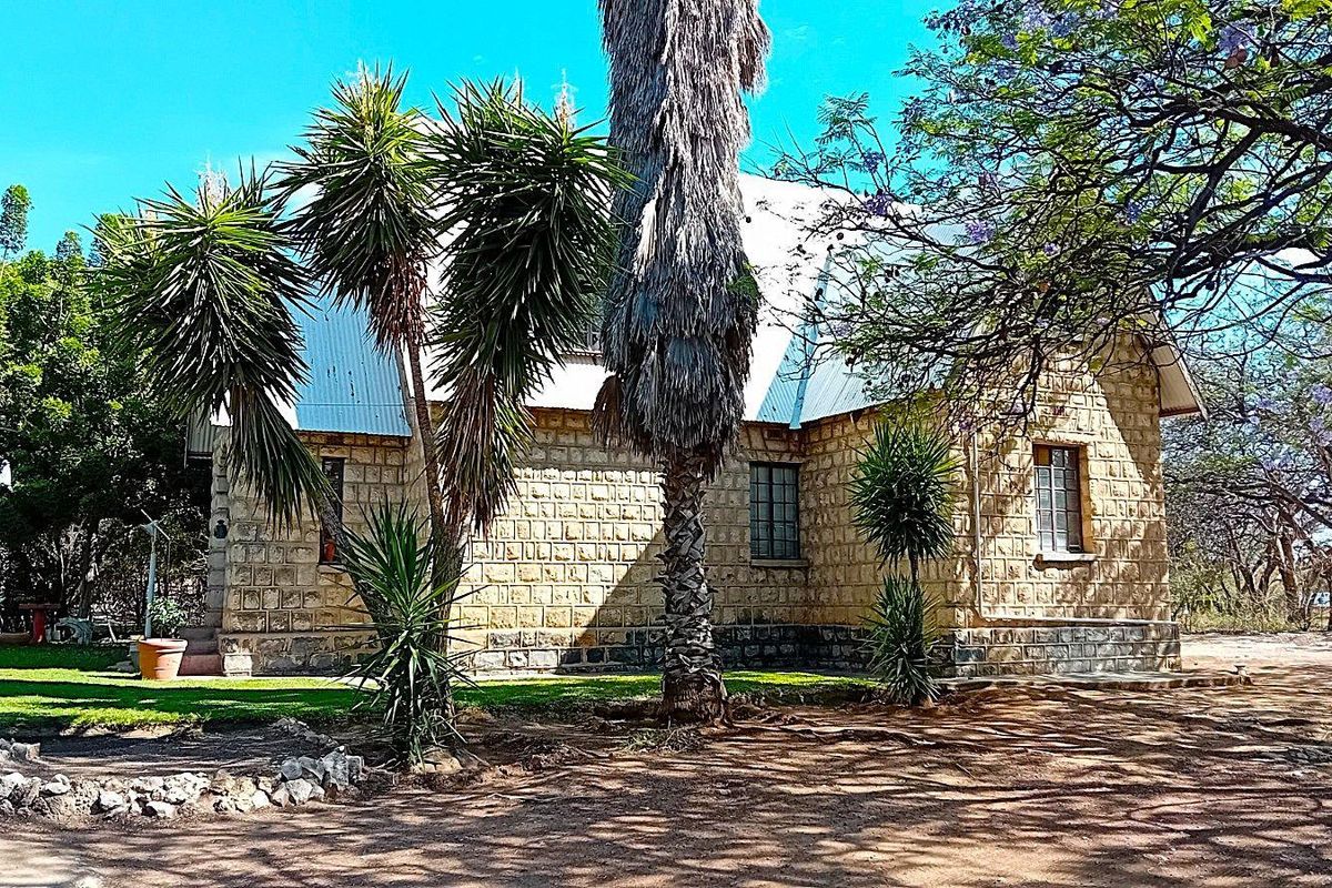 Rear view of a stone-clad building featuring a corrugated metal roof and steel-framed windows, set within a mature garden landscape.