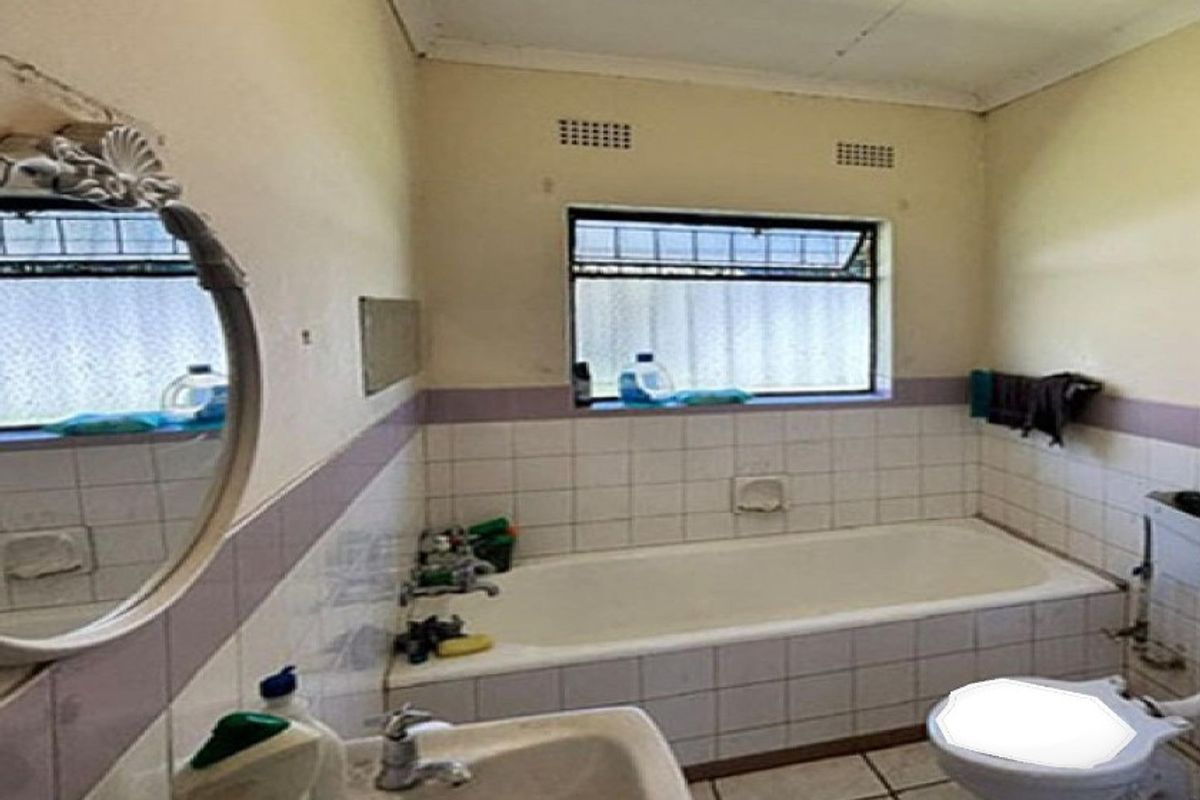 A dated bathroom featuring a built-in bathtub, pedestal basin, and toilet, with tiled splashbacks and a window for natural light.