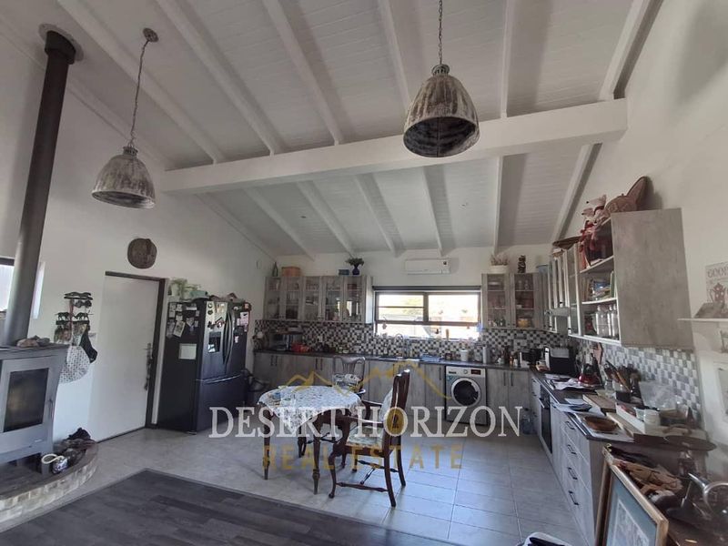 Spacious open-plan kitchen and living area featuring exposed beam ceilings, a wood-burning fireplace, and ample fitted cabinetry.
