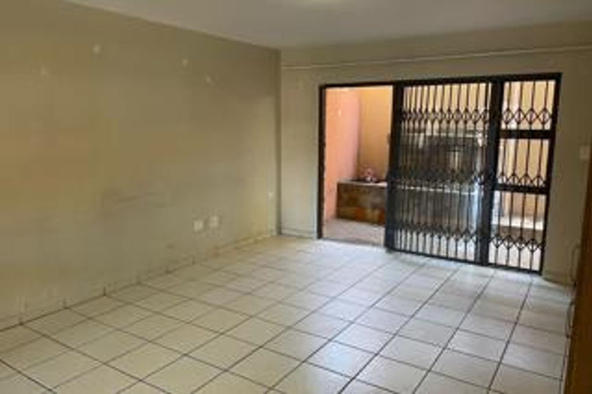 An empty living room featuring tiled flooring and a security gate leading to an outdoor area, requiring cosmetic updates to the wall finishes.