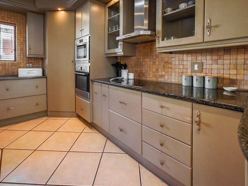 A functional kitchen featuring granite countertops, built-in oven and microwave, ceramic hob, extractor fan, and tiled flooring with a decorative backsplash.