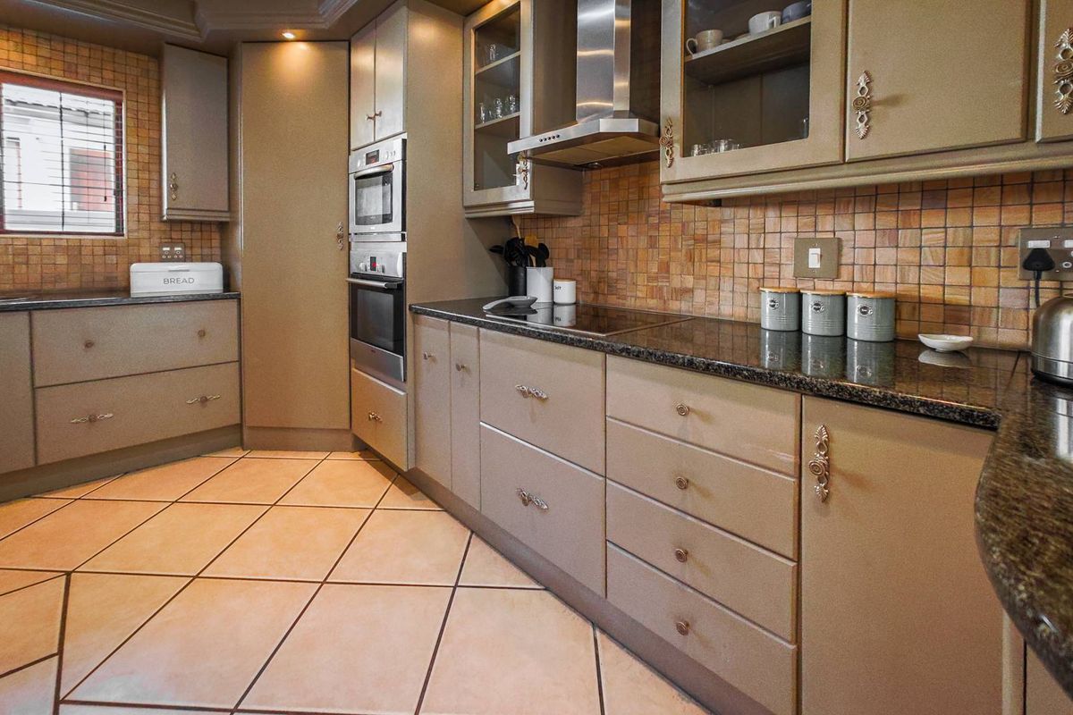 A functional kitchen featuring granite countertops, built-in oven and microwave, ceramic hob, extractor fan, and tiled flooring with a decorative backsplash.
