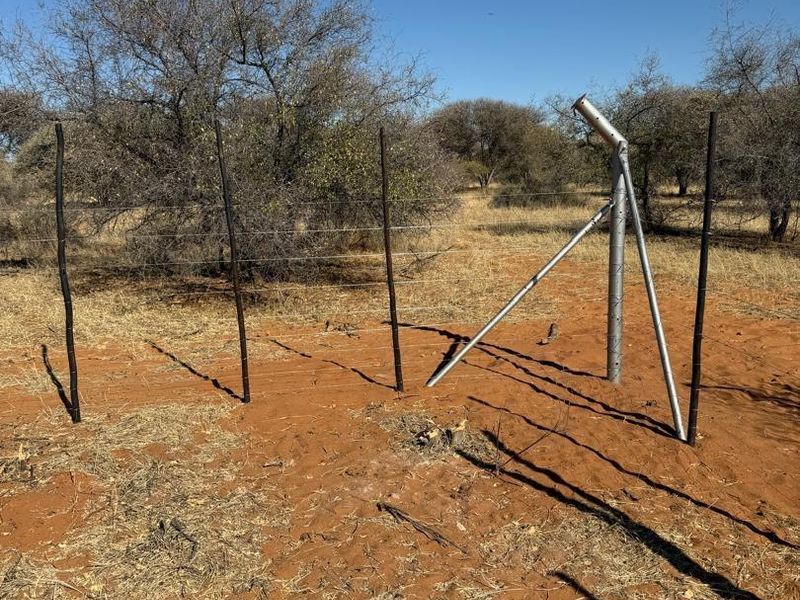 A view of agricultural land featuring a section of wire fencing with a damaged and leaning metal support post.
