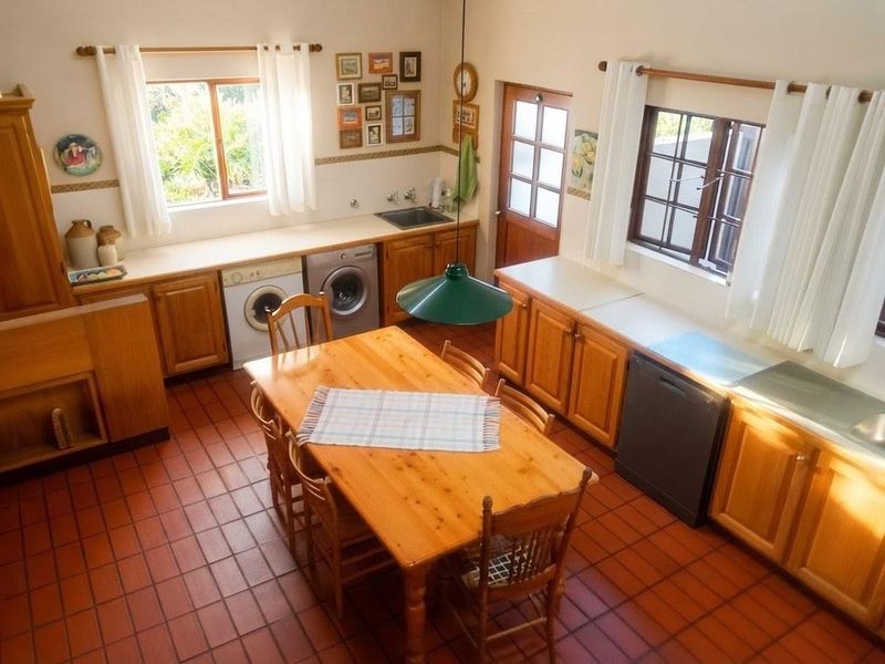 A spacious kitchen featuring traditional wooden cabinetry, terracotta tiled flooring, and ample natural light from multiple timber-framed windows.