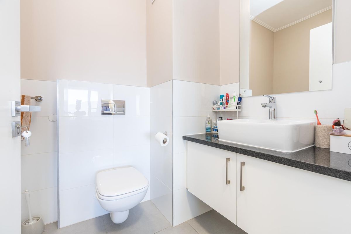 A modern bathroom featuring a wall-mounted toilet, a sleek vanity with a stone countertop, a vessel sink, and a large wall mirror.