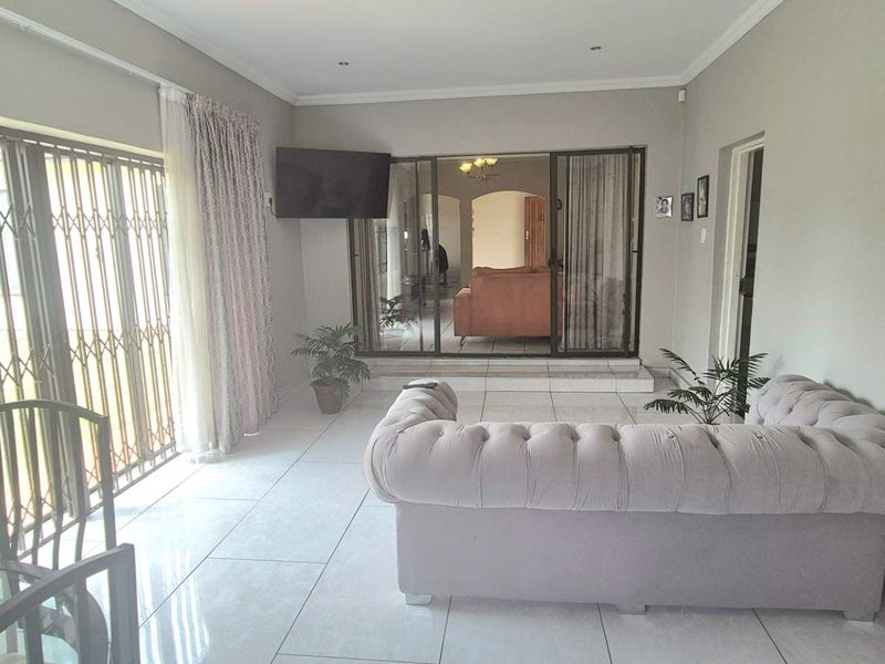 A bright living room featuring large sliding glass doors with security gates, neutral tiled flooring, and recessed ceiling lighting.