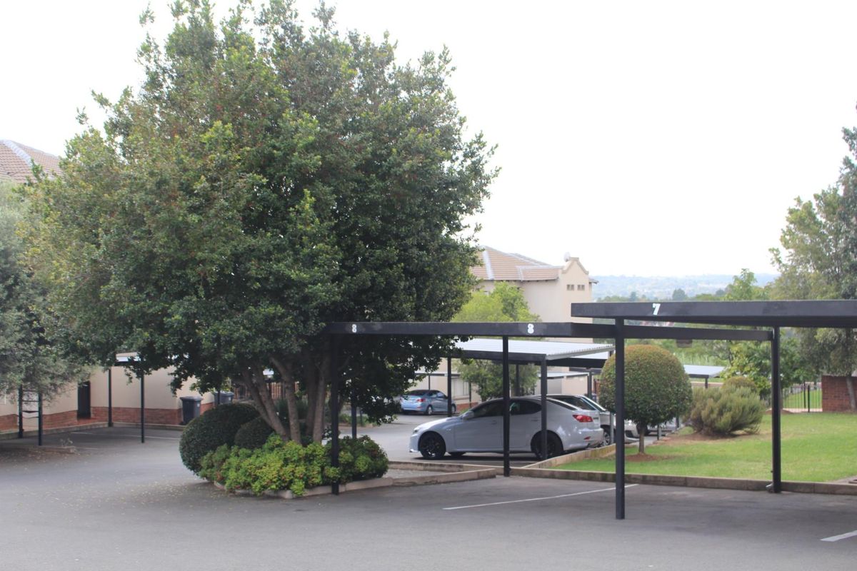 A view of the apartment complex parking area featuring covered carports and established landscaping.