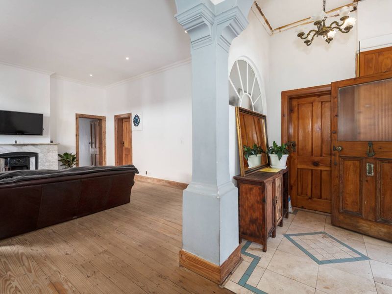 Spacious living area featuring original wooden floors, a marble fireplace, and a distinct architectural pillar separating the entrance from the main lounge space.