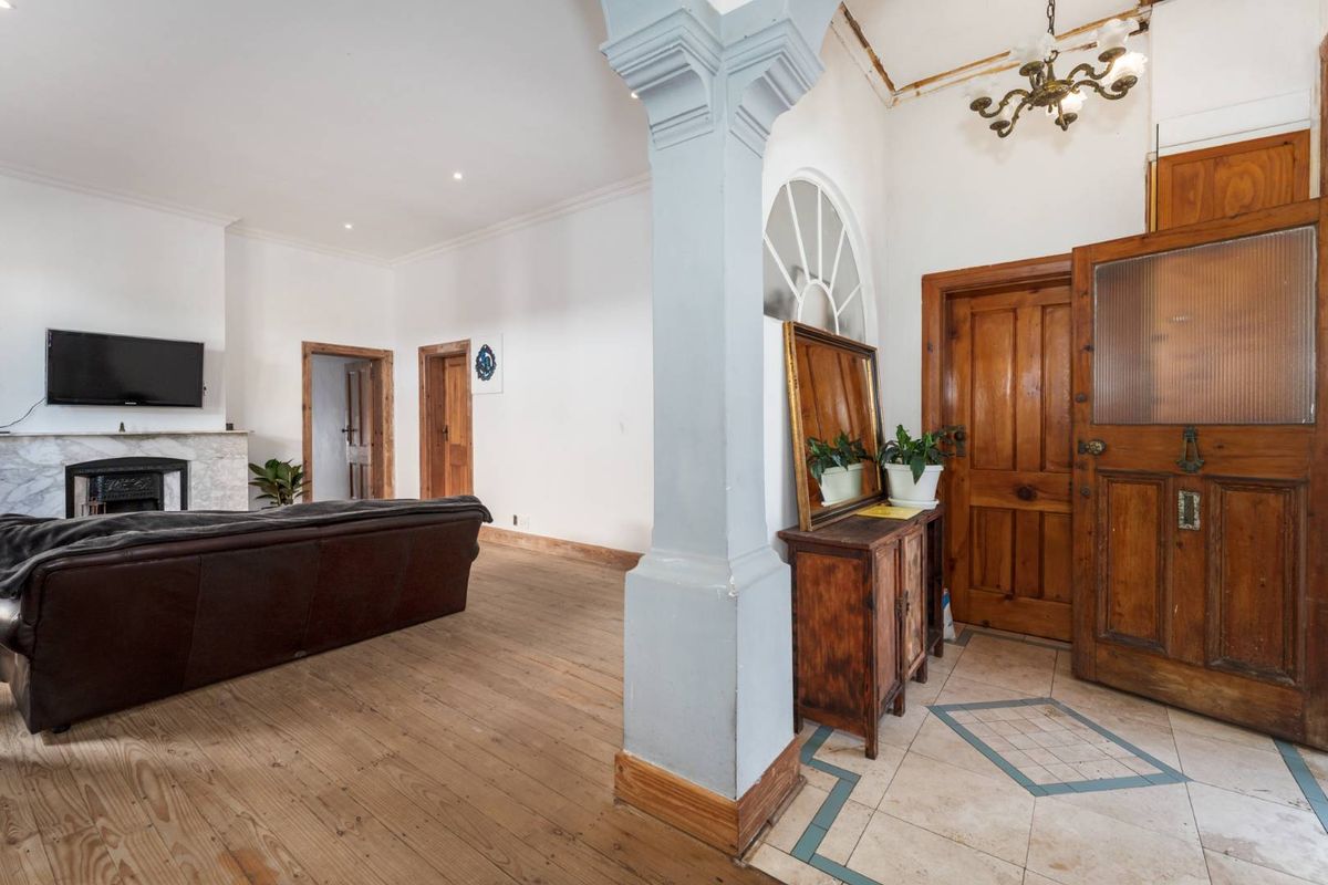 Spacious living area featuring original wooden floors, a marble fireplace, and a distinct architectural pillar separating the entrance from the main lounge space.