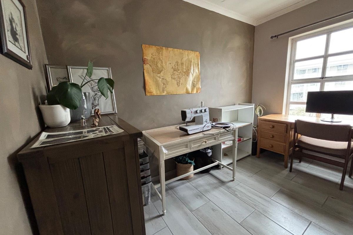 A functional bedroom or home office space featuring tiled flooring, neutral wall tones, and natural light from a multi-pane window.