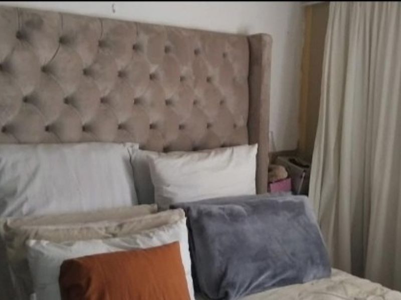 A bedroom interior featuring a large tufted headboard and floor-to-ceiling curtains.