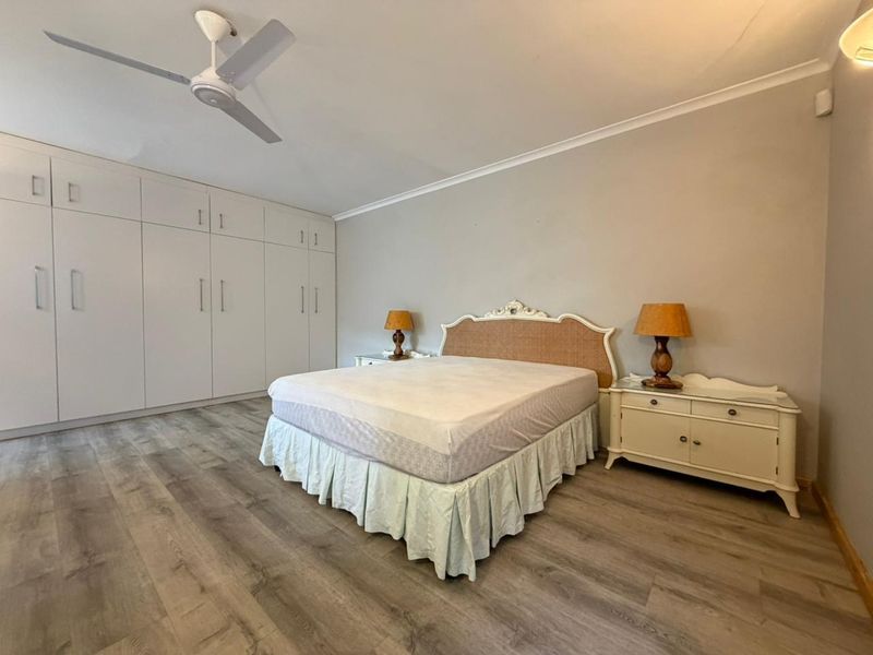 Spacious bedroom featuring modern laminate flooring, extensive built-in cabinetry for storage, and a ceiling fan.