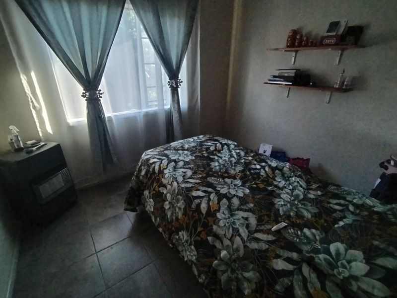 A bedroom featuring tiled flooring, a window with curtains, and wall-mounted shelving units.