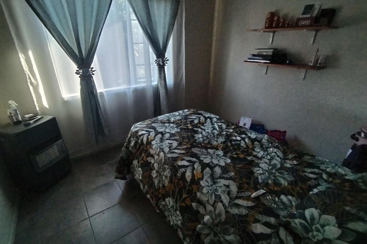 A bedroom featuring tiled flooring, a window with curtains, and wall-mounted shelving units.