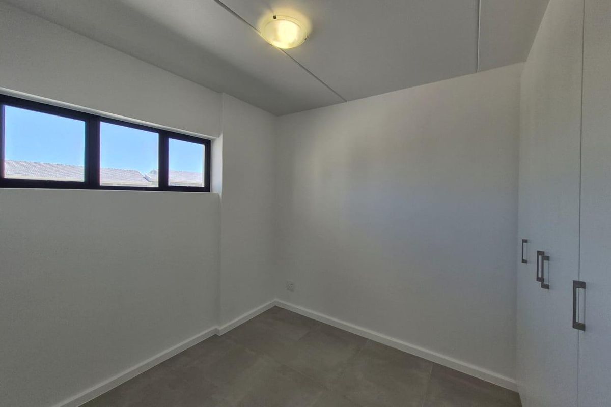 A clean, empty bedroom featuring neutral floor tiles, built-in cupboards, and a horizontal window providing natural light.
