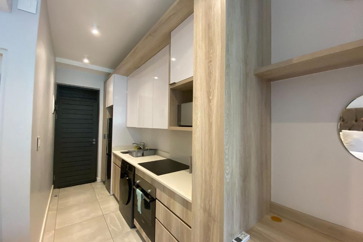 Modern compact kitchen featuring sleek wood-grain and white cabinetry, integrated appliances, stone-look countertops, and tiled flooring in a clean, contemporary apartment setting.
