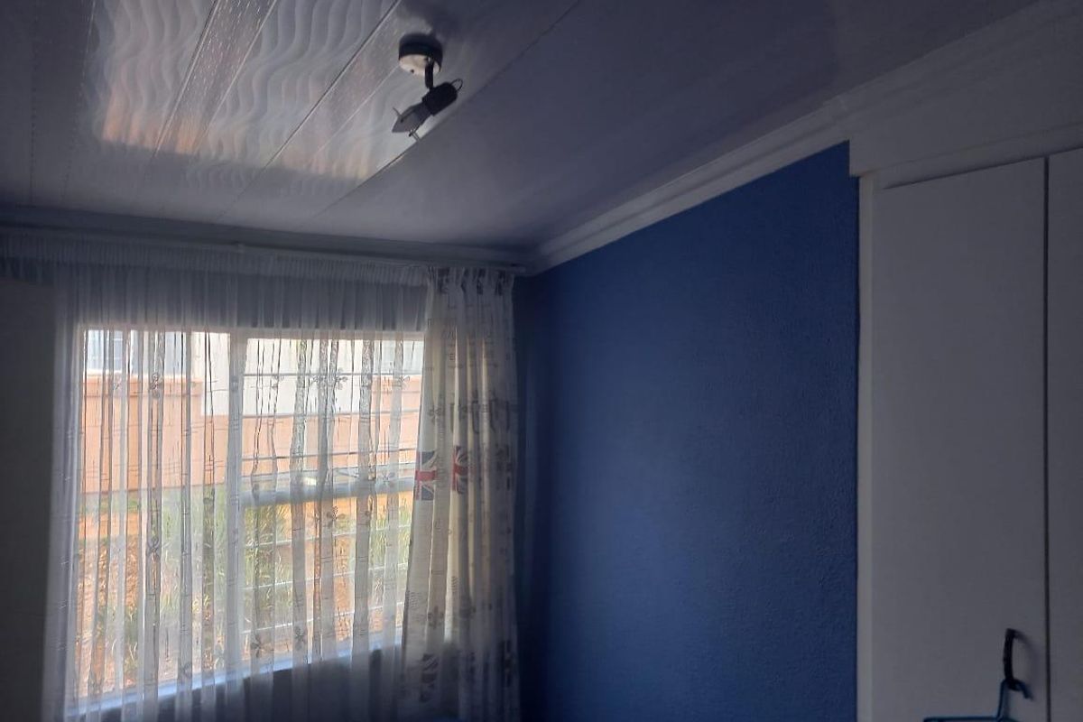 A bedroom featuring a built-in wardrobe, textured ceiling panels, and a window with security bars.