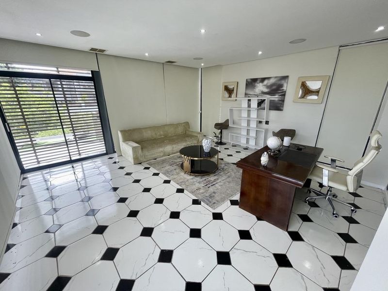 A modern office space featuring high-contrast patterned floor tiles, recessed lighting, and a large sliding glass door providing natural light and outdoor access.
