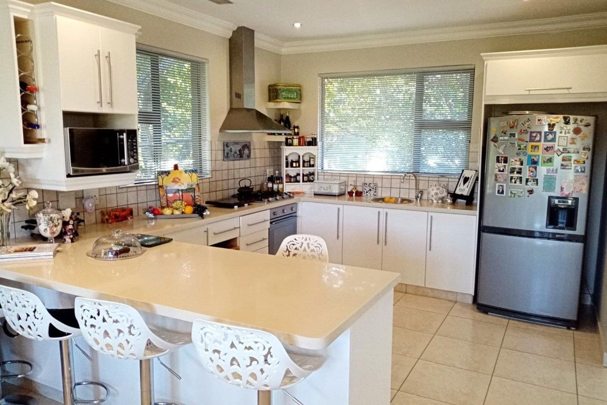 A functional kitchen featuring white cabinetry, stone countertops, a breakfast bar, stainless steel appliances, and tiled flooring with ample natural light.