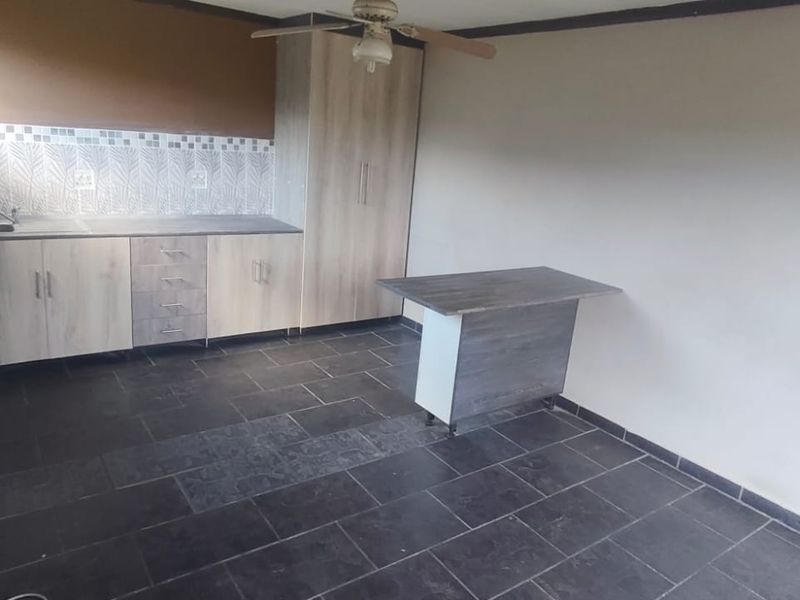 A functional kitchen area featuring built-in cabinetry, laminate countertops, a stainless steel sink, and dark tiled flooring.