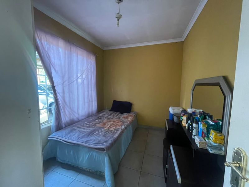 A compact bedroom featuring tiled flooring, coved ceilings, and a window with security bars, currently requiring cosmetic updates to the wall finishes.