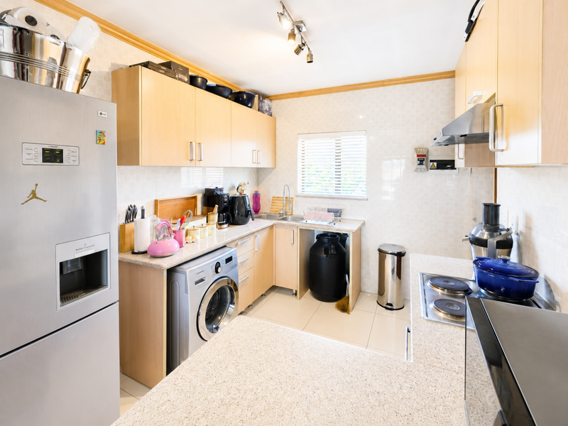 Functional kitchen featuring light wood cabinetry, stone-look laminate countertops, tiled backsplash, and integrated appliance space with a built-in electric hob and extractor.