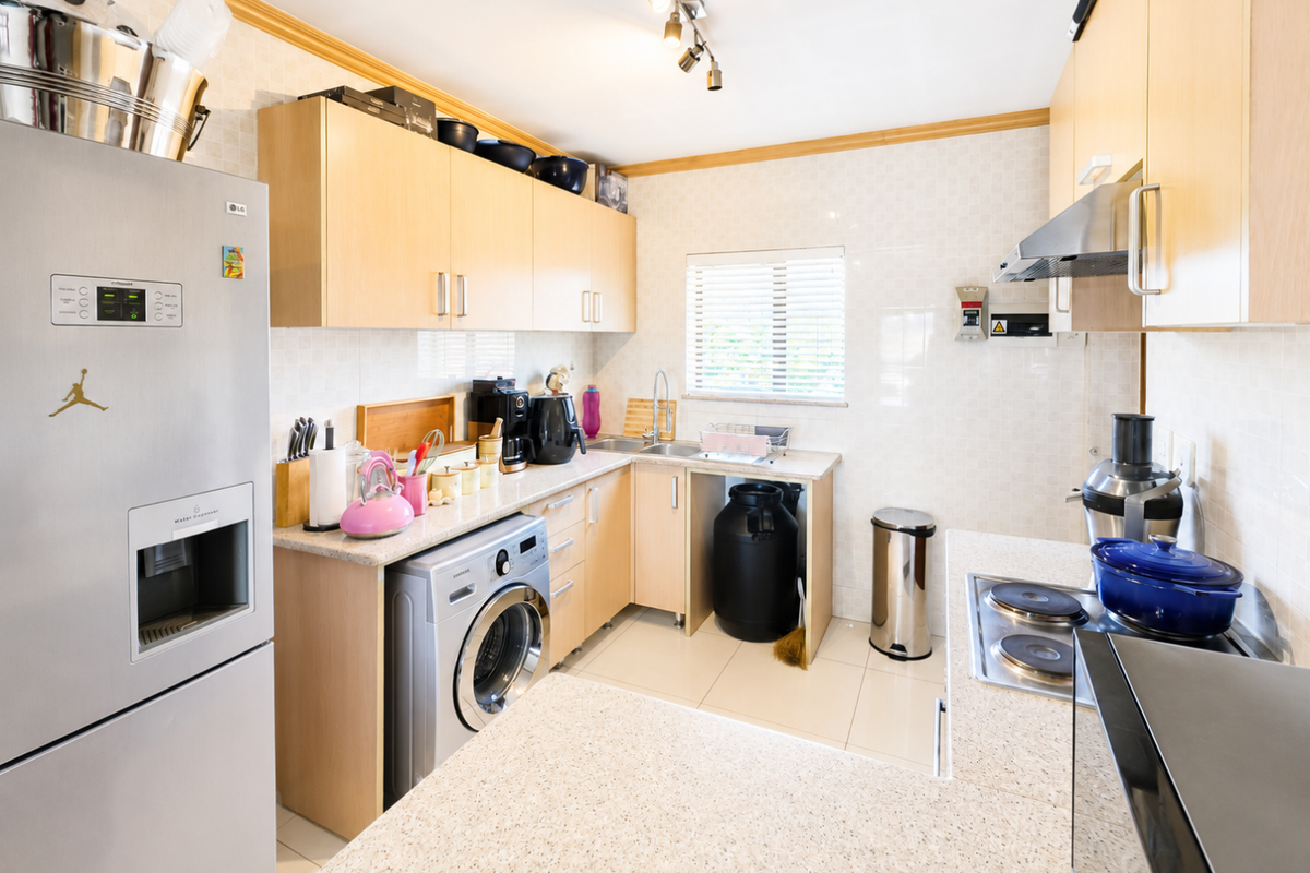 Functional kitchen featuring light wood cabinetry, stone-look laminate countertops, tiled backsplash, and integrated appliance space with a built-in electric hob and extractor.