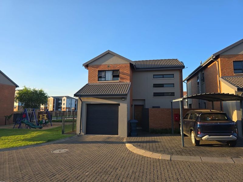 Front elevation of a modern townhouse featuring a brick and plaster facade, single garage, and an adjacent carport with paved driveway.