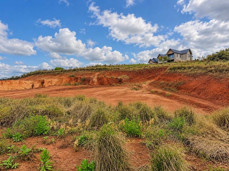 A view of a vacant commercial land plot featuring excavated earth banks and natural sloped terrain with surrounding vegetation.