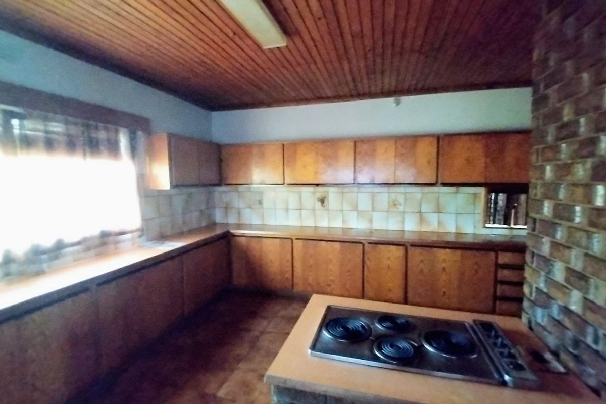 A dated kitchen featuring wooden cabinetry, a brick feature wall, and a timber ceiling, offering significant potential for a modern renovation.