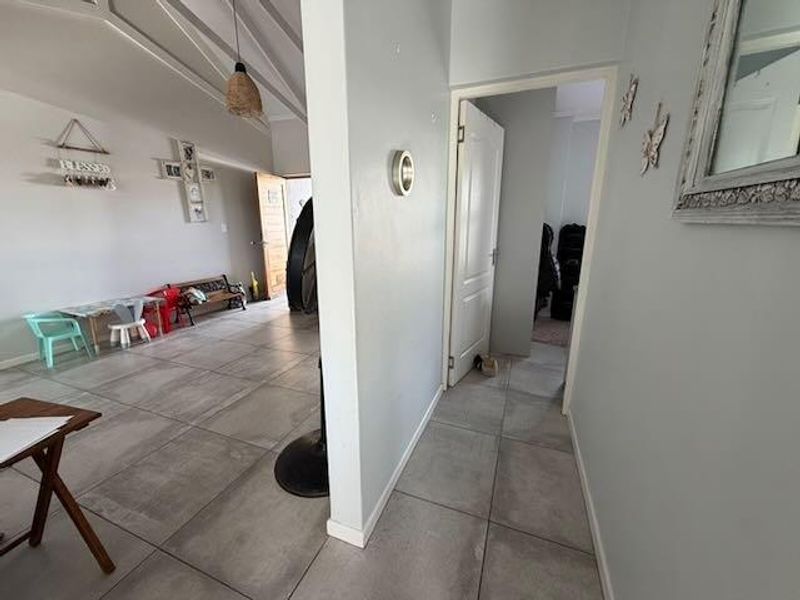 A bright hallway featuring large format floor tiles and a vaulted ceiling, providing access to adjacent living areas and rooms.