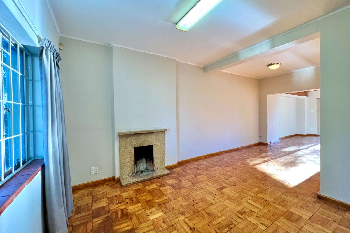 Spacious living room featuring original parquet flooring and a central stone fireplace, offering a blank canvas for modern interior design updates.