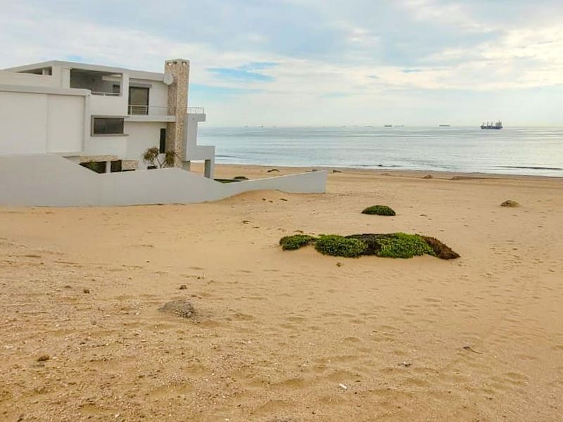 A modern residential property situated directly on the beachfront, featuring a stone chimney and balcony with expansive ocean views.