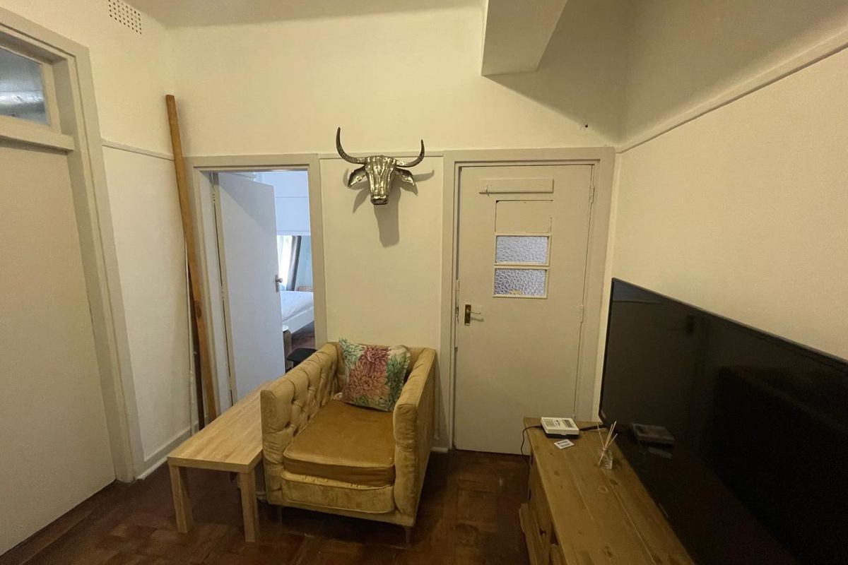 A living room area featuring original parquet flooring, high ceilings with picture rails, and access to an adjoining bedroom.