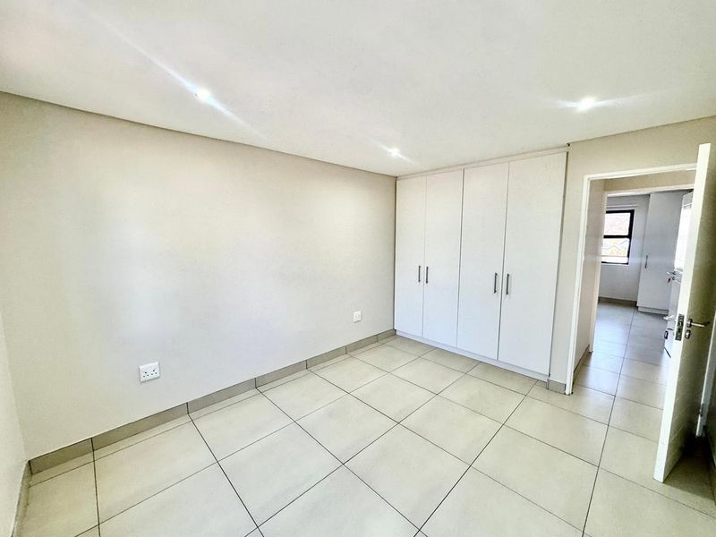 A bright, empty bedroom featuring neutral tiled flooring, recessed ceiling lighting, and ample built-in cupboard storage space.