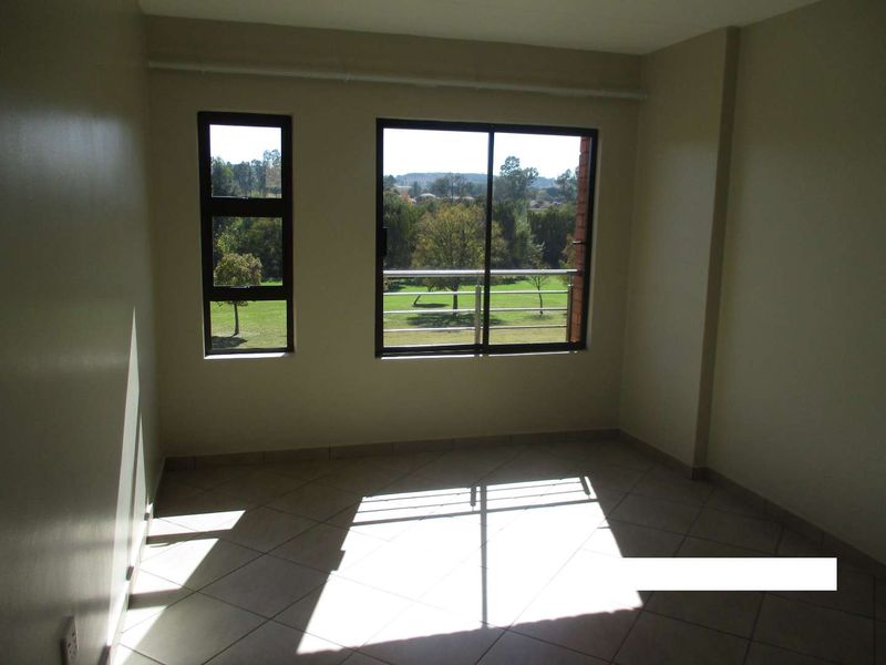 An empty bedroom featuring tiled flooring, aluminium window frames, and a sliding glass door leading to a balcony with scenic views.