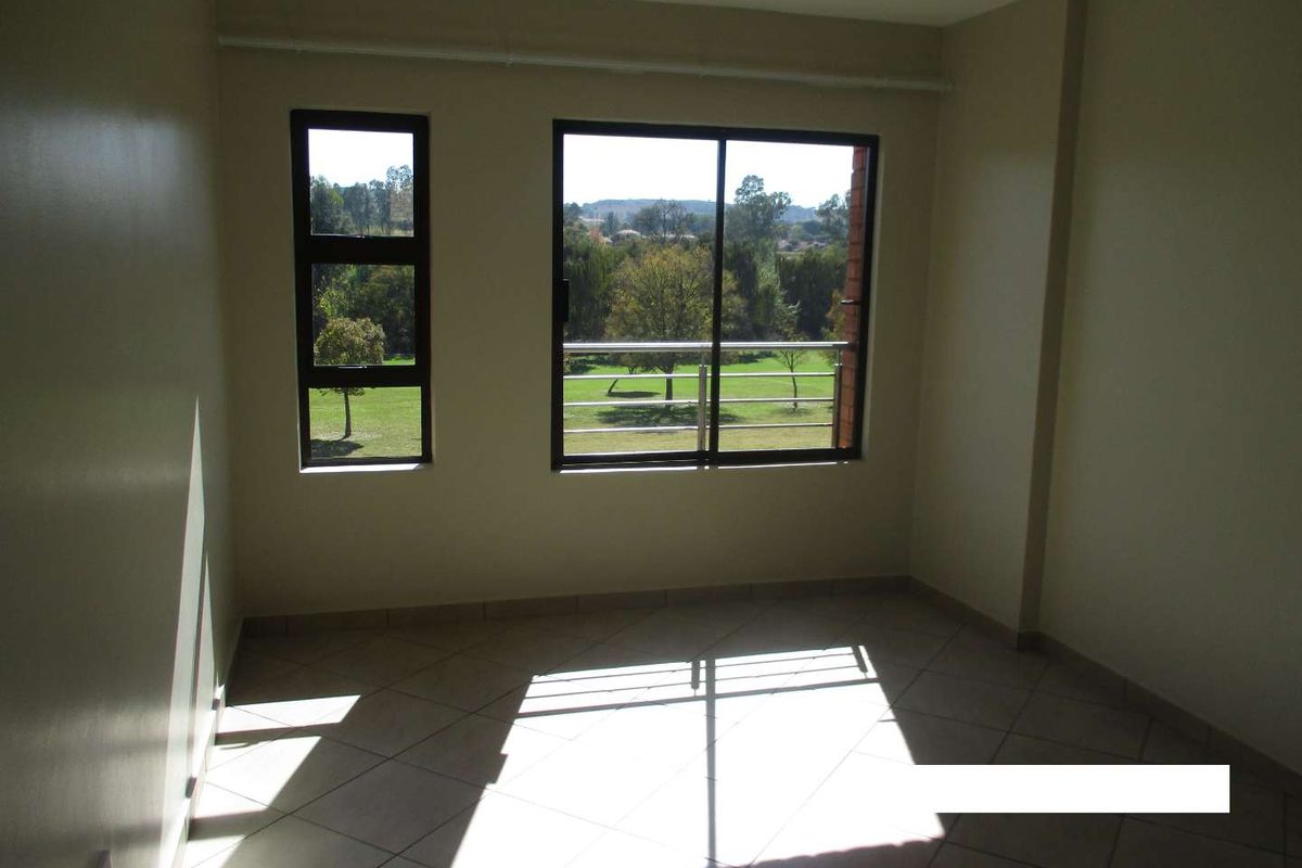An empty bedroom featuring tiled flooring, aluminium window frames, and a sliding glass door leading to a balcony with scenic views.