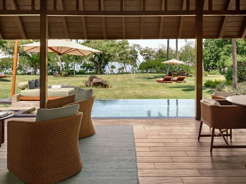 A luxurious covered patio featuring timber decking and ceiling, overlooking a private infinity pool and expansive landscaped garden with ocean views.